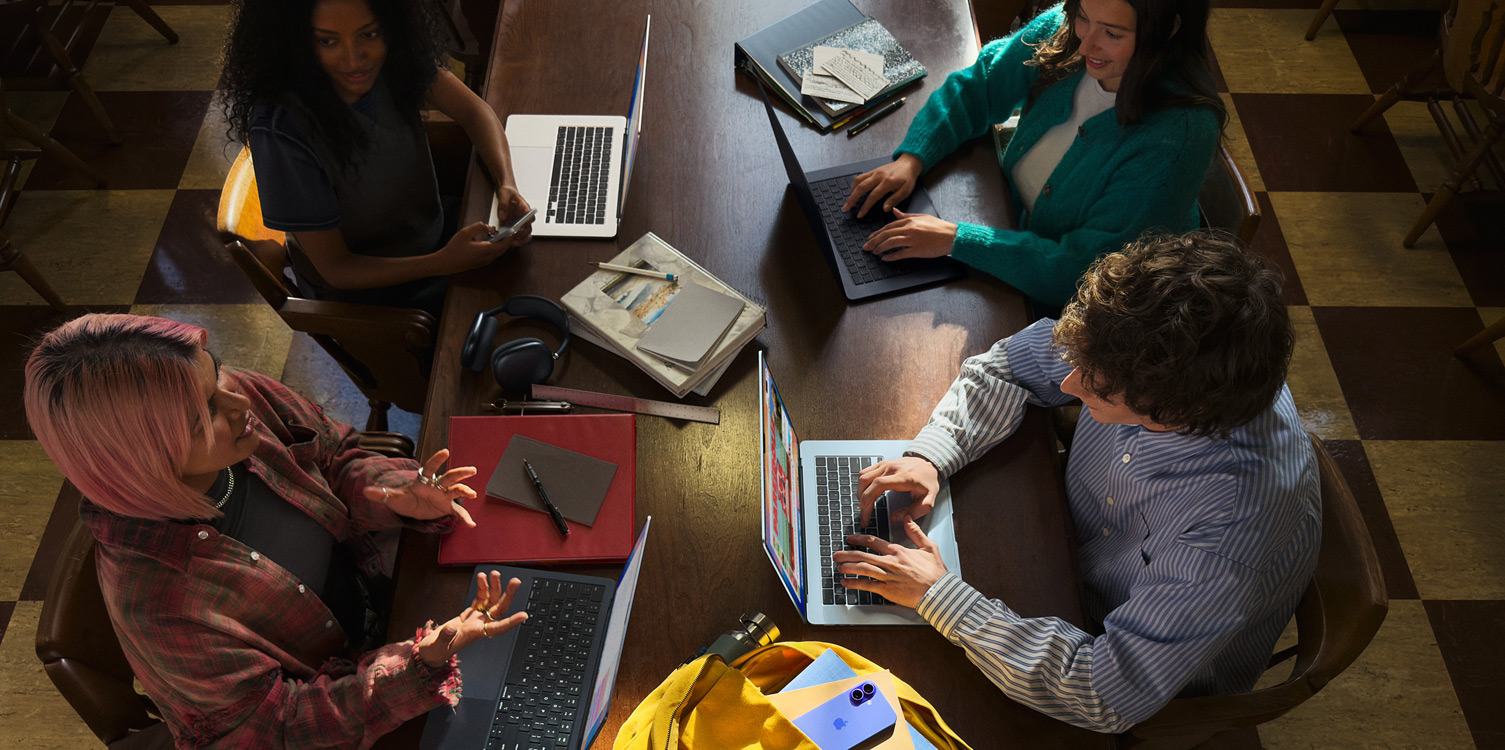 Quatro estudantes sentados a uma mesa, com portáteis MacBook e apontamentos abertos à sua frente.
