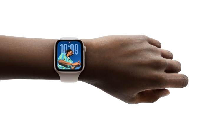 Close-up of Apple Watch in Rose Gold with rubber band on a person’s wrist, showing Time app in new Liquid Glass design