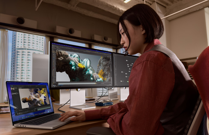 En person jobber i et kontorlandskap med en MacBook Pro koblet til Studio Display XDR